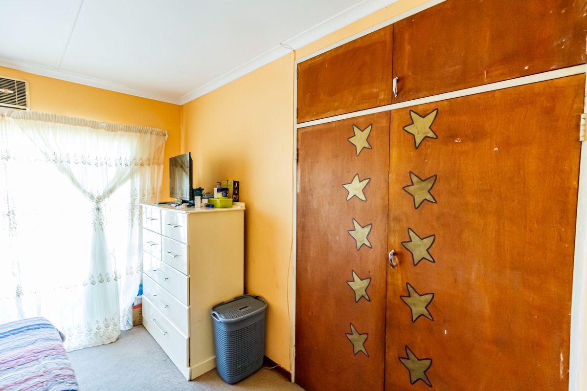 A bedroom featuring built-in wooden cupboards, carpeted flooring, and an integrated air conditioning unit, requiring cosmetic updates to modernize the space.