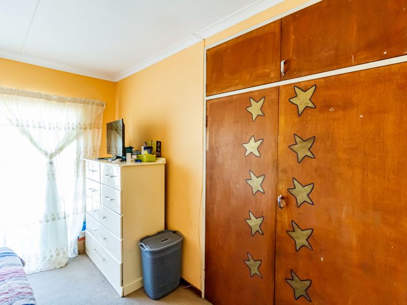 A bedroom featuring built-in wooden cupboards, carpeted flooring, and an integrated air conditioning unit, requiring cosmetic updates to modernize the space.