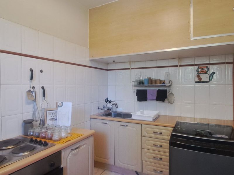 A functional kitchen featuring built-in cabinetry, laminate countertops, a stainless steel sink, and an integrated electric hob and oven with tiled backsplash.