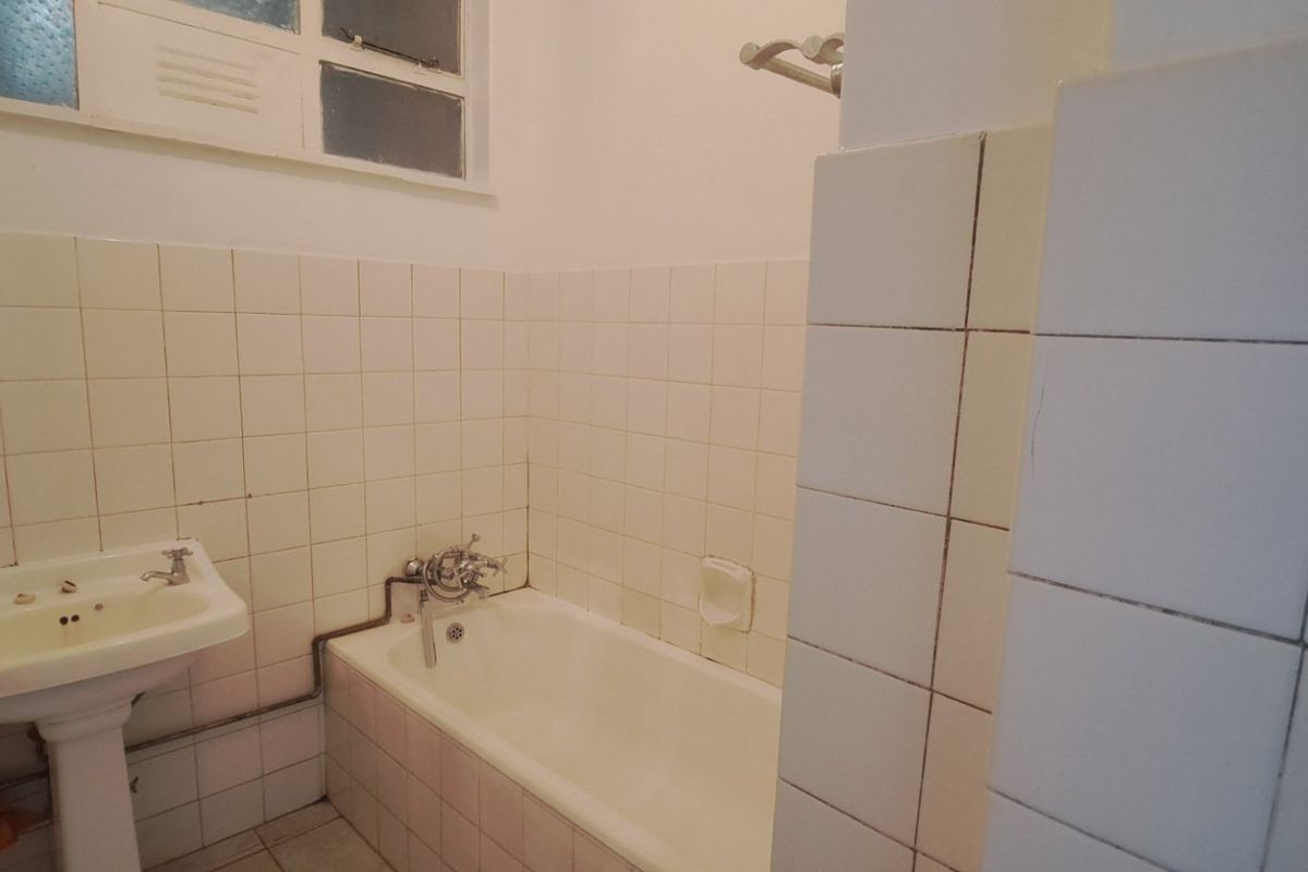 A dated bathroom featuring a pedestal washbasin, bathtub with wall-mounted mixer, and ceramic wall tiling. The space is ready for modernization.