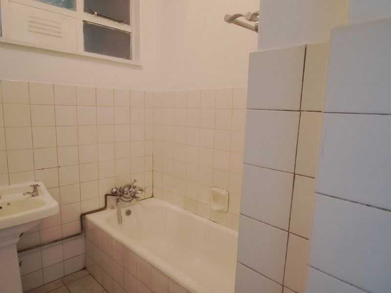 A dated bathroom featuring a pedestal washbasin, bathtub with wall-mounted mixer, and ceramic wall tiling. The space is ready for modernization.