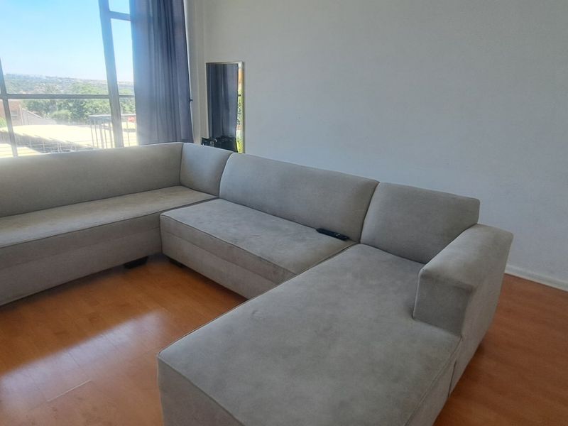 A bright living room featuring large floor-to-ceiling windows that provide ample natural light and views, complemented by warm-toned laminate flooring.