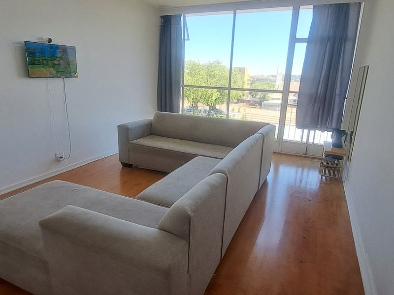 A bright living room featuring laminate flooring and a large floor-to-ceiling window providing natural light and access to the balcony.