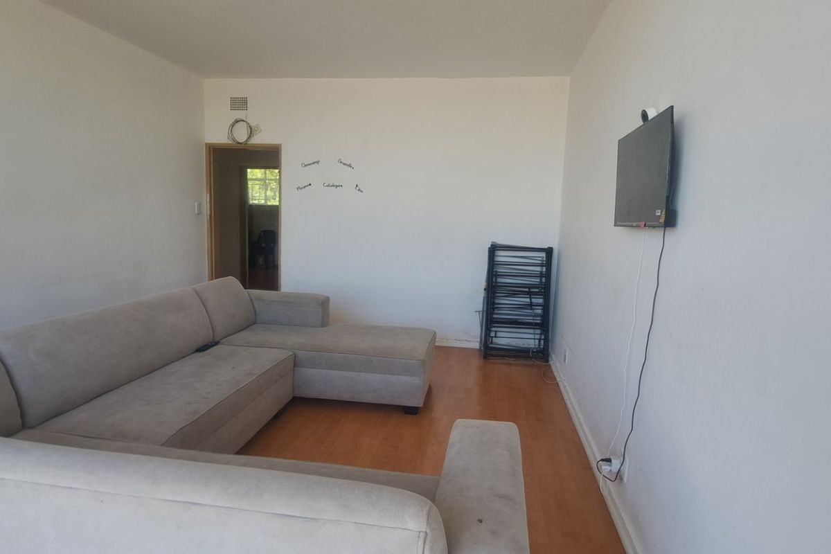 A living room featuring laminate flooring and a wall-mounted television setup, offering a blank canvas for potential interior design updates.
