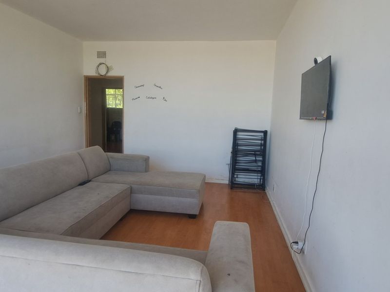 A living room featuring laminate flooring and a wall-mounted television setup, offering a blank canvas for potential interior design updates.