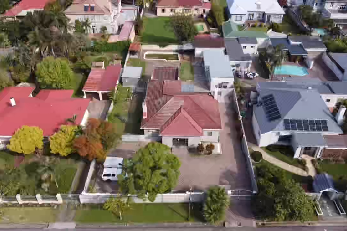 Aerial view of a residential property featuring a tiled roof, paved driveway, and boundary wall, situated within a suburban neighborhood.