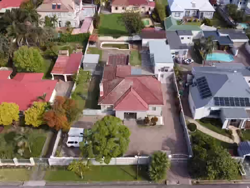 Aerial view of a residential property featuring a tiled roof, paved driveway, and boundary wall, situated within a suburban neighborhood.