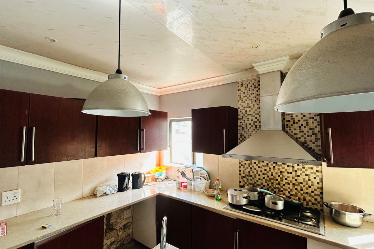 A functional kitchen featuring dark wood cabinetry, stone countertops, a mosaic tile backsplash, and a stainless steel extractor fan with integrated gas hob.