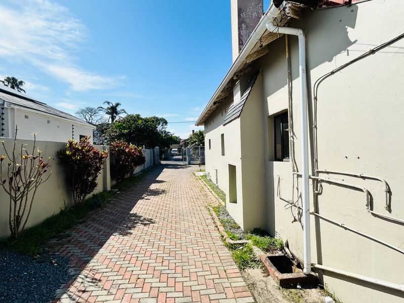 A narrow paved side passage along the exterior of the commercial building, featuring exposed plumbing and boundary walling.