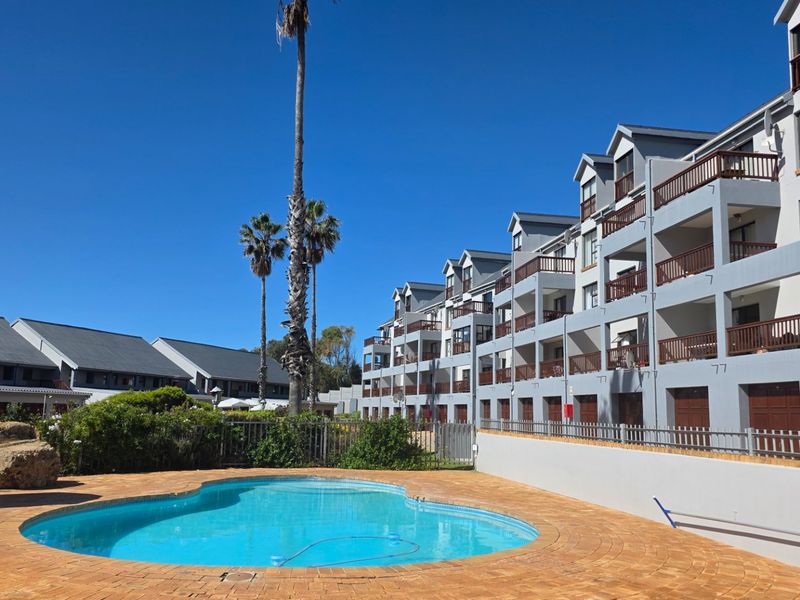 A well-maintained communal swimming pool area featuring brick paving, surrounded by multi-story apartment blocks with private balconies and established landscaping.