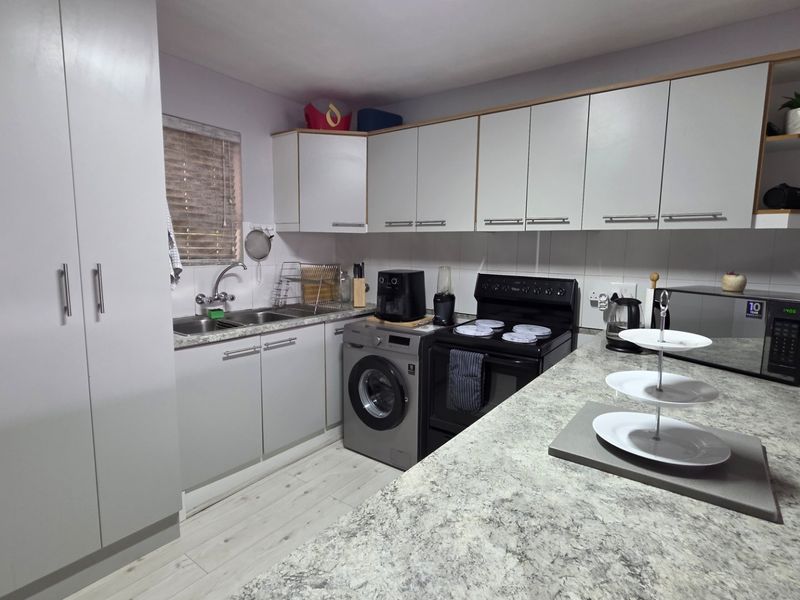 A functional kitchen featuring light-toned cabinetry, stone-look laminate countertops, a tiled backsplash, and integrated laundry facilities.