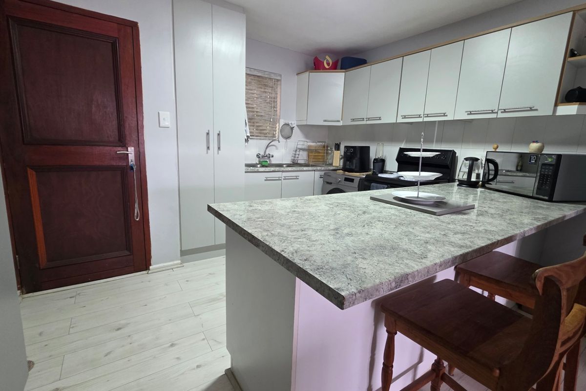 A functional kitchen featuring laminate countertops, ample built-in cabinetry, a stainless steel sink, and a tiled backsplash, finished with light-toned laminate flooring.