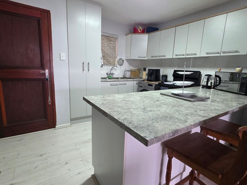 A functional kitchen featuring laminate countertops, ample built-in cabinetry, a stainless steel sink, and a tiled backsplash, finished with light-toned laminate flooring.