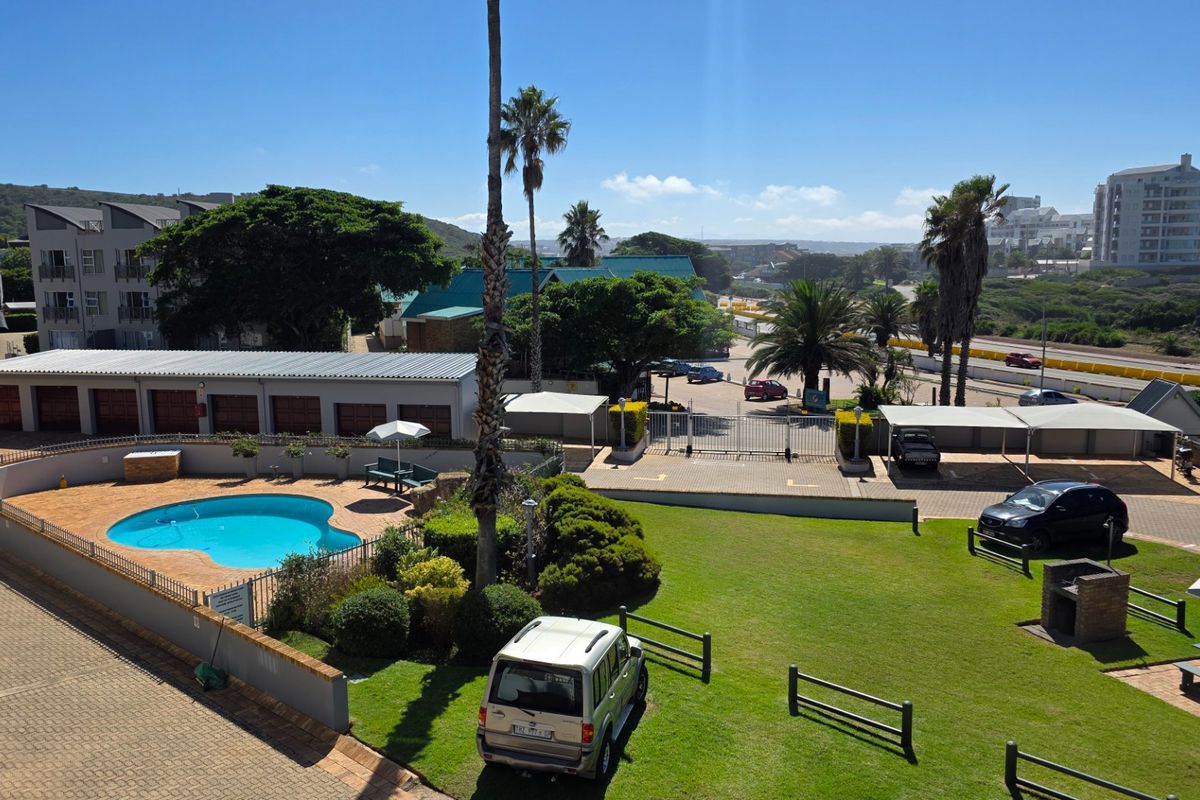 Aerial view of the apartment complex grounds featuring a swimming pool, landscaped lawn, paved parking areas, and communal braai facilities.