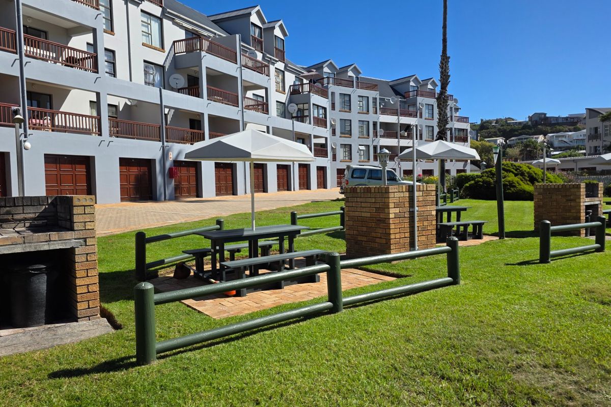 Communal garden area featuring brick braai stands, paved picnic spots, and well-maintained lawns set against the apartment complex facade.