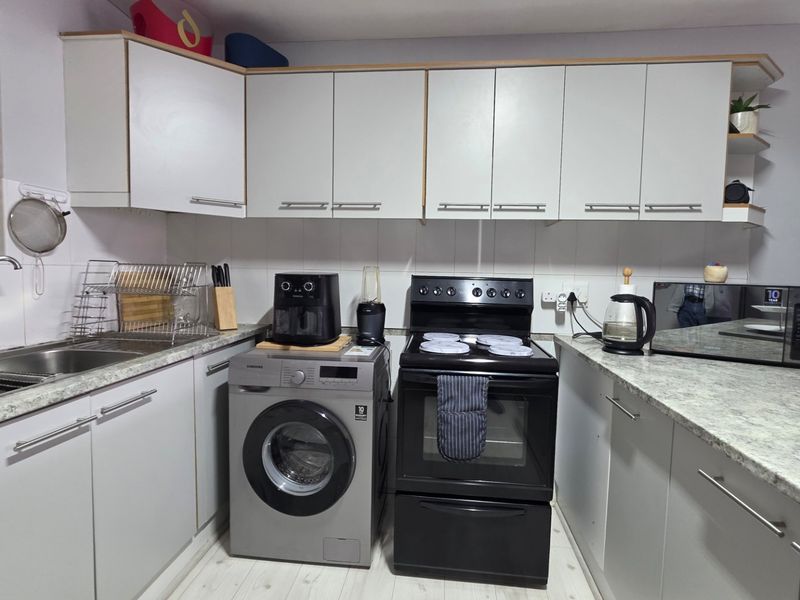 A functional kitchen featuring white cabinetry, laminate countertops, a tiled backsplash, and space for a washing machine and freestanding oven.