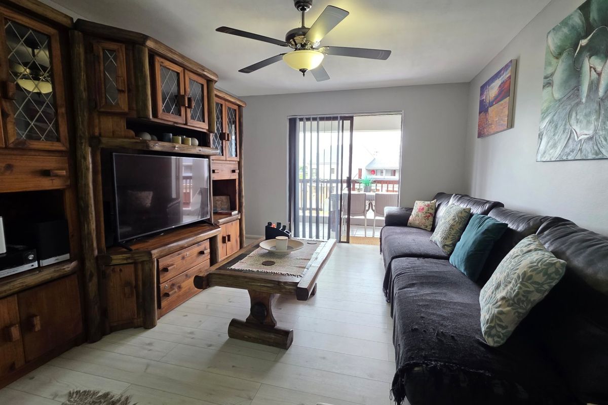 A comfortable living room featuring light-toned laminate flooring, a ceiling fan, and a sliding glass door providing access to an outdoor balcony area.