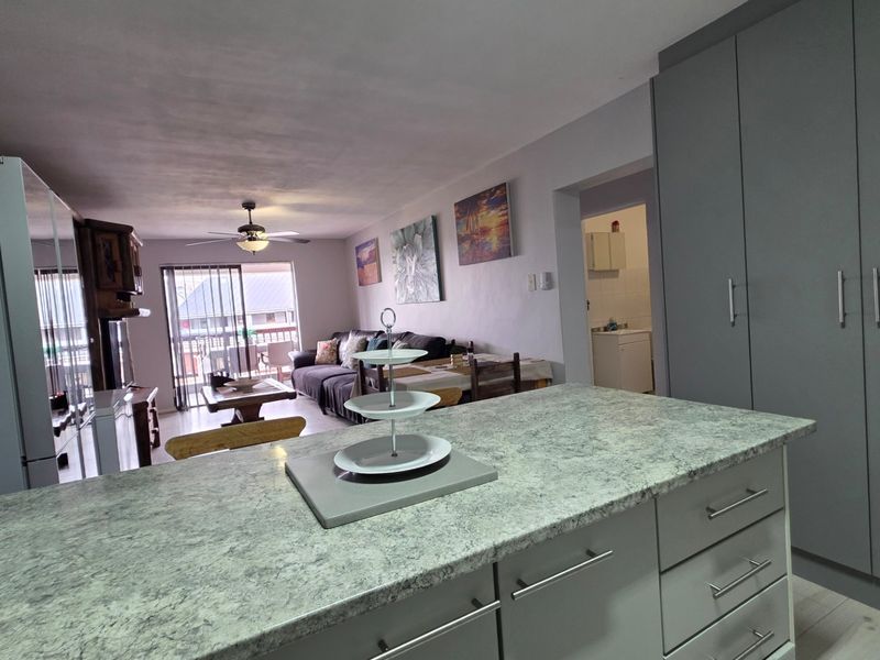 Open-plan living area featuring a modern kitchen island with laminate countertops, ample built-in cabinetry, and seamless flow to the adjacent living space and balcony.