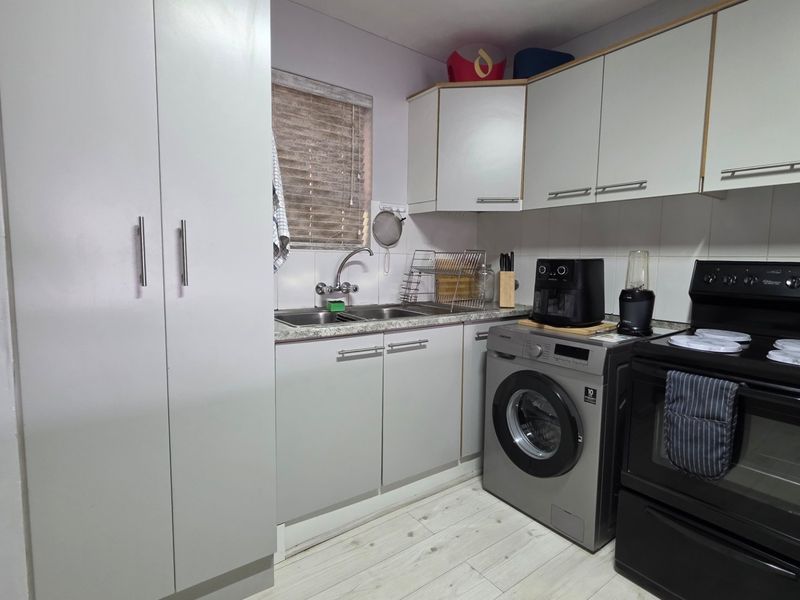 Compact kitchen featuring light-toned cabinetry, laminate countertops, tiled backsplash, and integrated space for a washing machine and freestanding oven.