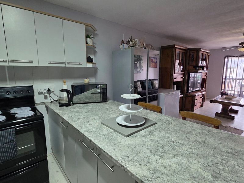 Open-plan kitchen and living area featuring built-in cabinetry, laminate countertops, an electric stove, and access to a balcony through sliding glass doors.