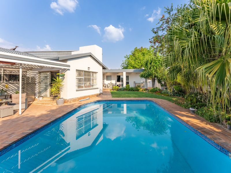 A well-maintained backyard featuring a sparkling swimming pool, brick-paved surround, and a covered patio area adjacent to the main house.