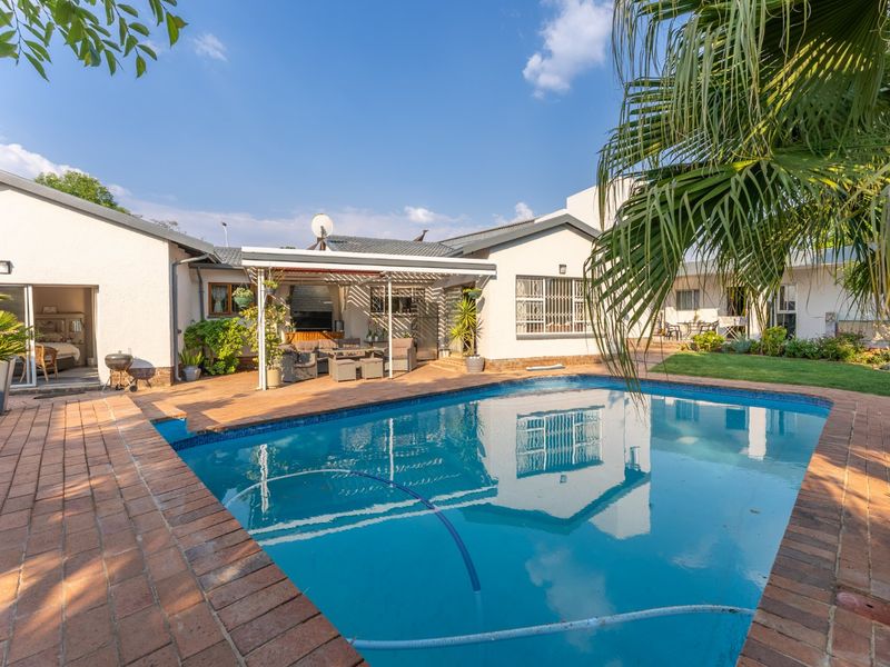 A well-maintained outdoor pool area featuring brick paving, a covered patio space, and established garden surroundings, ideal for outdoor relaxation and entertainment.