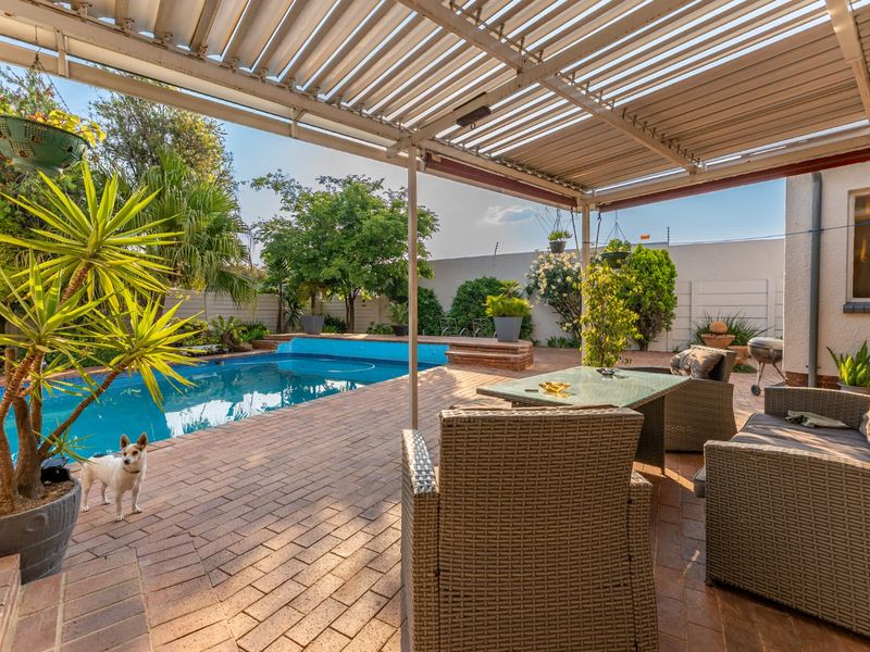 Outdoor entertainment area featuring a swimming pool and a covered patio with a louvre roof pergola, set within a private garden.