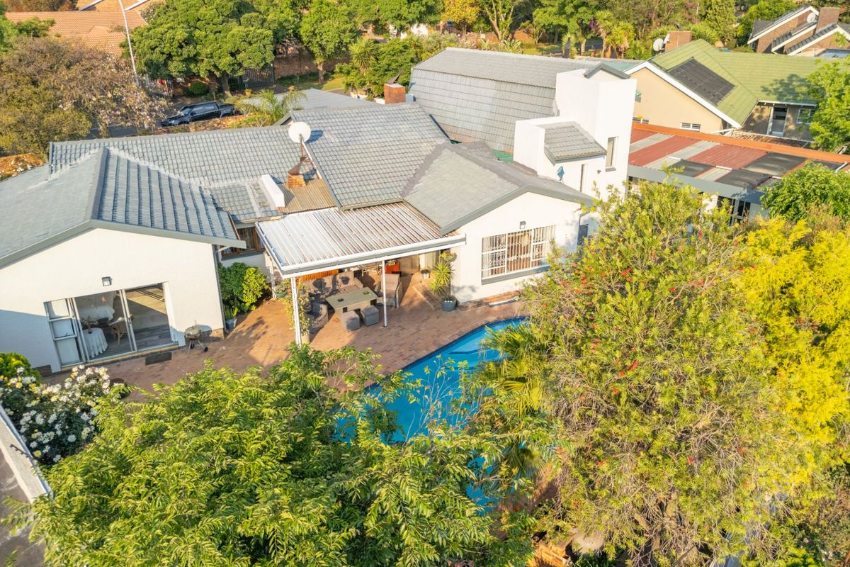 Aerial view of the property featuring a tiled roof, a swimming pool, and a covered patio area with brick paving.
