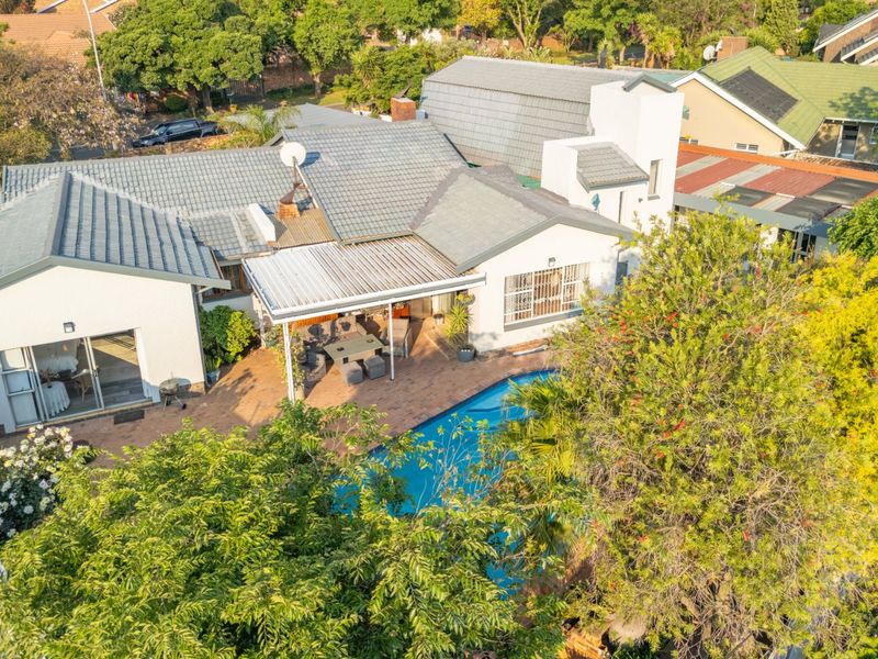 Aerial view of the property featuring a tiled roof, a swimming pool, and a covered patio area with brick paving.