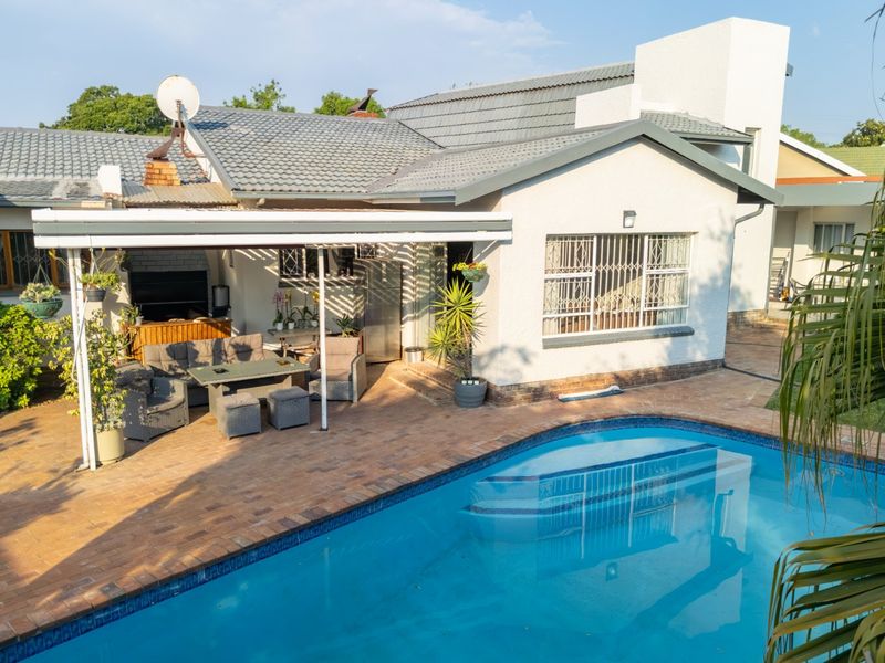 Outdoor entertainment area featuring a swimming pool, brick-paved patio, and a covered space with a built-in braai.