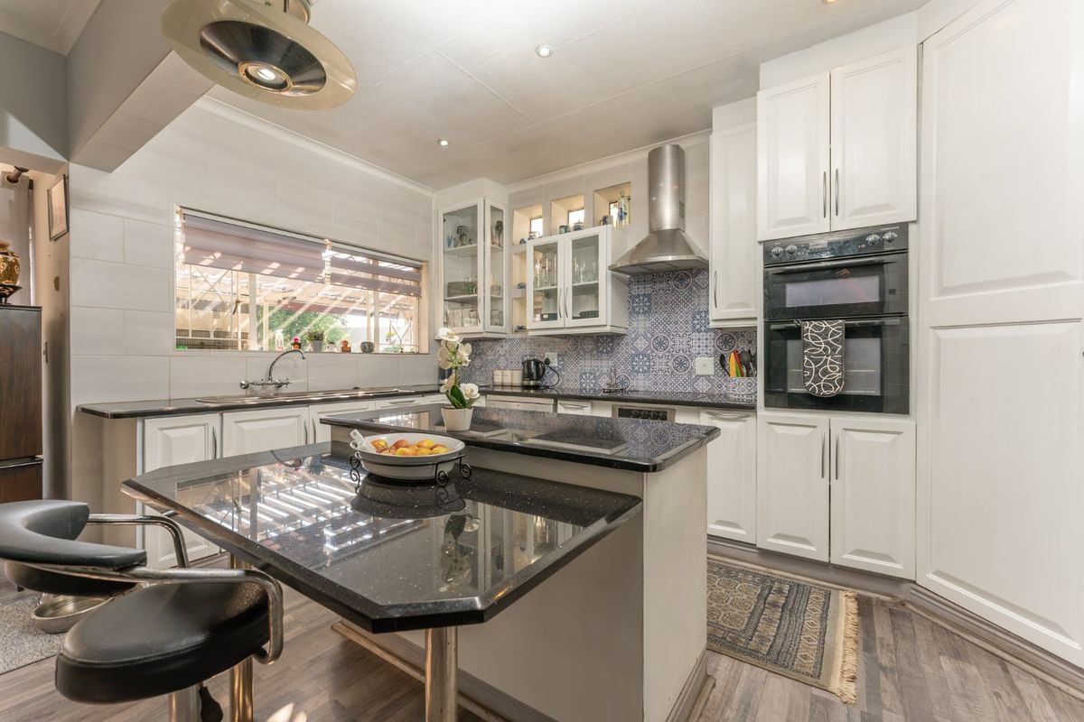 A well-appointed kitchen featuring white cabinetry, black granite countertops, a central island, and integrated stainless steel appliances with a decorative tiled backsplash.