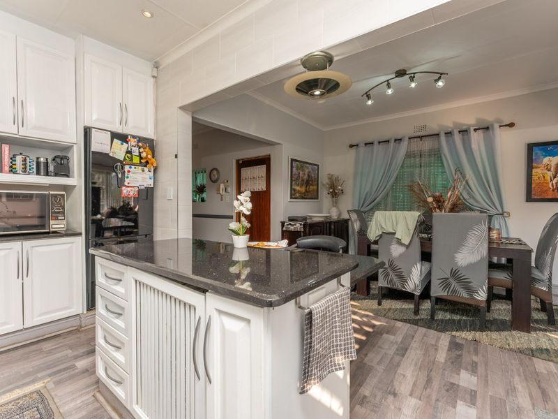 Open-plan kitchen and dining area featuring white cabinetry, a granite-topped island, and modern laminate flooring, creating a functional and connected living space.