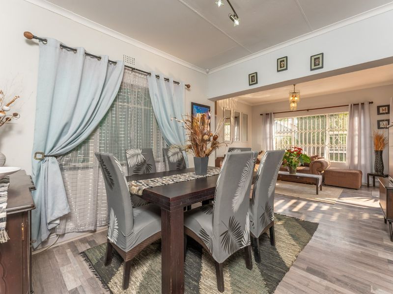 Open plan dining and living area featuring laminate flooring, track lighting, and large windows with security gates.