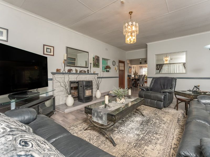 A spacious living room featuring a stone fireplace, chair rail molding, and a central chandelier, providing a comfortable and traditional living space.