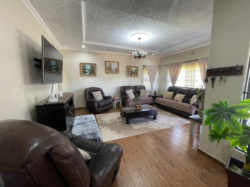 Spacious living room featuring decorative ceiling tiles, a central chandelier, and warm laminate flooring, creating a comfortable and inviting atmosphere.