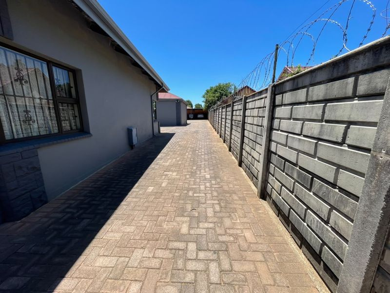 A paved side driveway leading to the rear of the property, featuring a secure precast concrete boundary wall with razor wire.