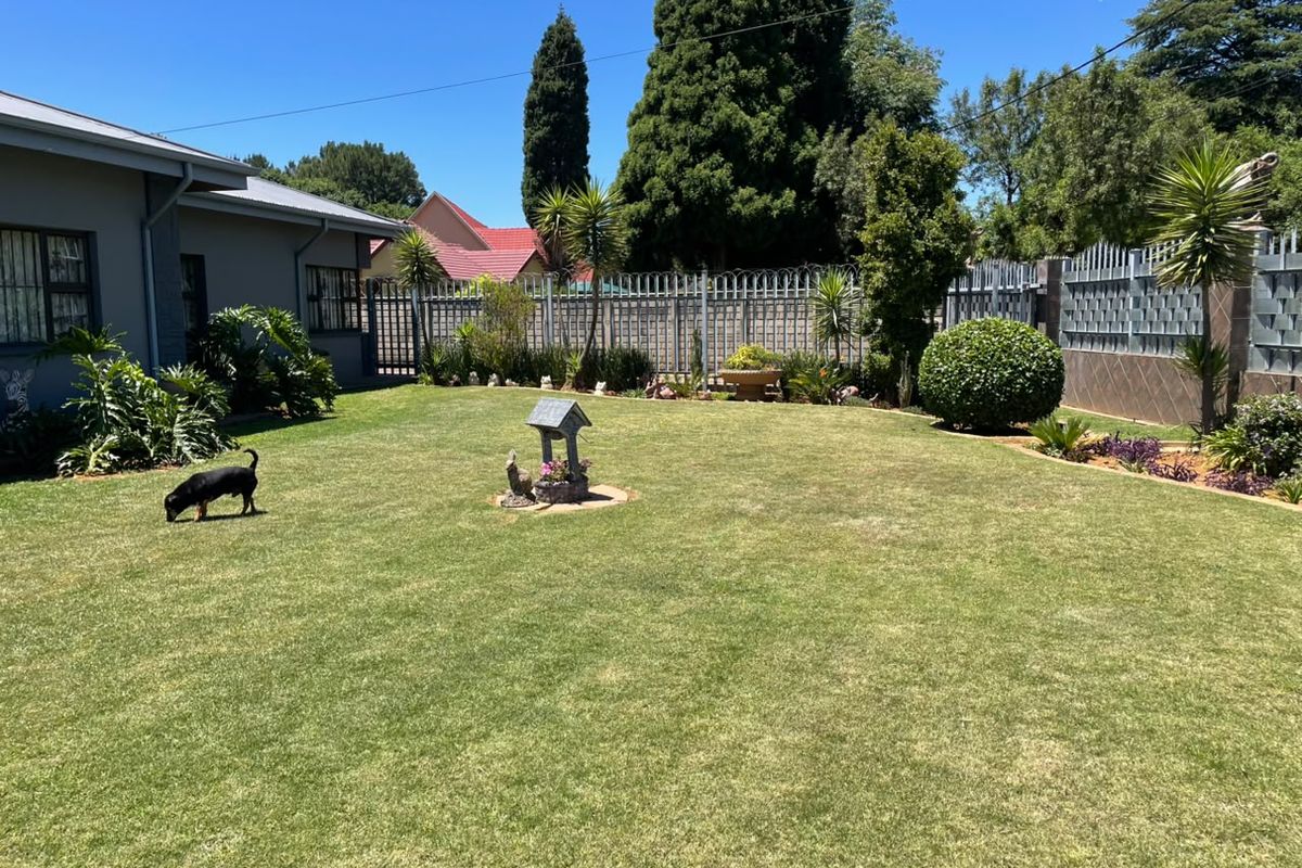 A well-maintained rear garden featuring a manicured lawn, established perimeter fencing with security features, and mature landscaping.