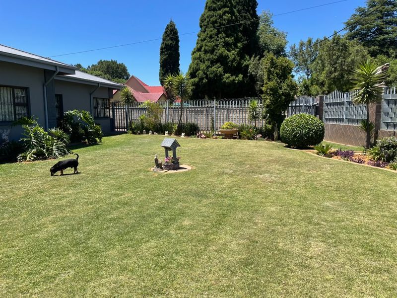A well-maintained rear garden featuring a manicured lawn, established perimeter fencing with security features, and mature landscaping.