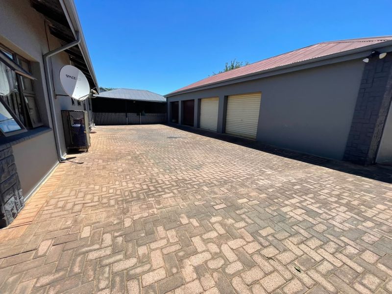 Spacious paved rear courtyard area featuring a triple garage with roller doors and well-maintained exterior walls.