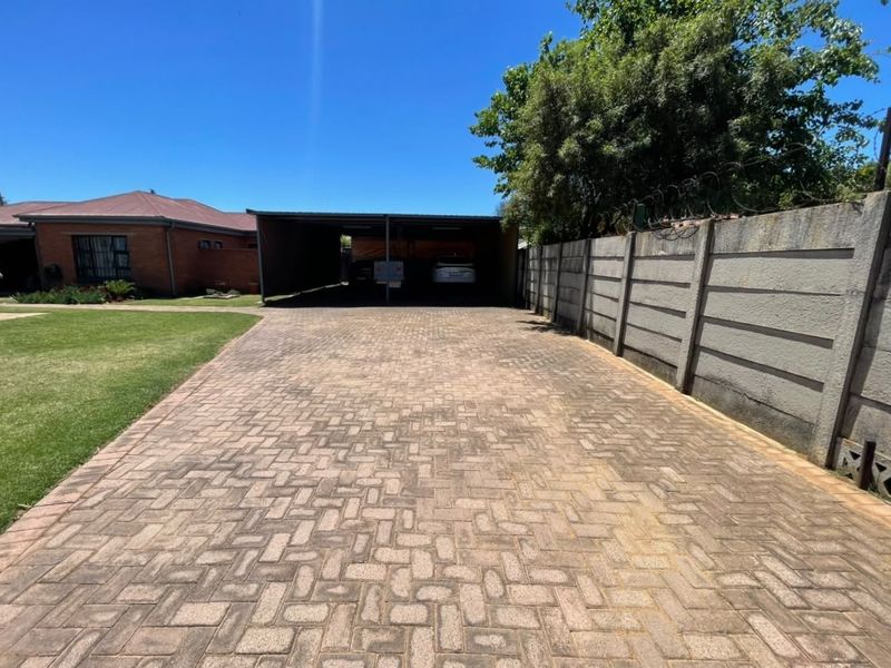 Front view of the property featuring a paved driveway leading to a carport, enclosed by a precast concrete boundary wall with security razor wire.