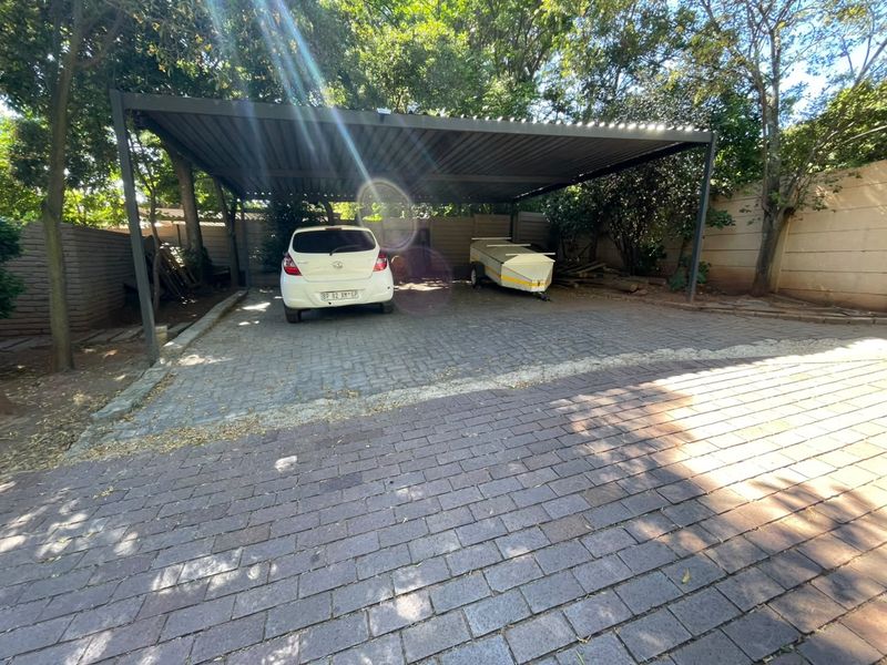 A covered carport area with paved driveway and surrounding boundary walls, providing secure off-street parking.