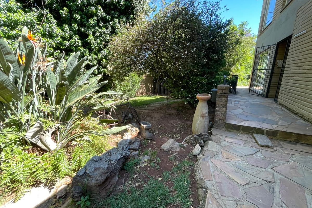 A rear garden area featuring a stone-paved patio, established greenery, and direct access to the home via a security gate.