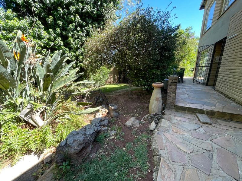 A rear garden area featuring a stone-paved patio, established greenery, and direct access to the home via a security gate.