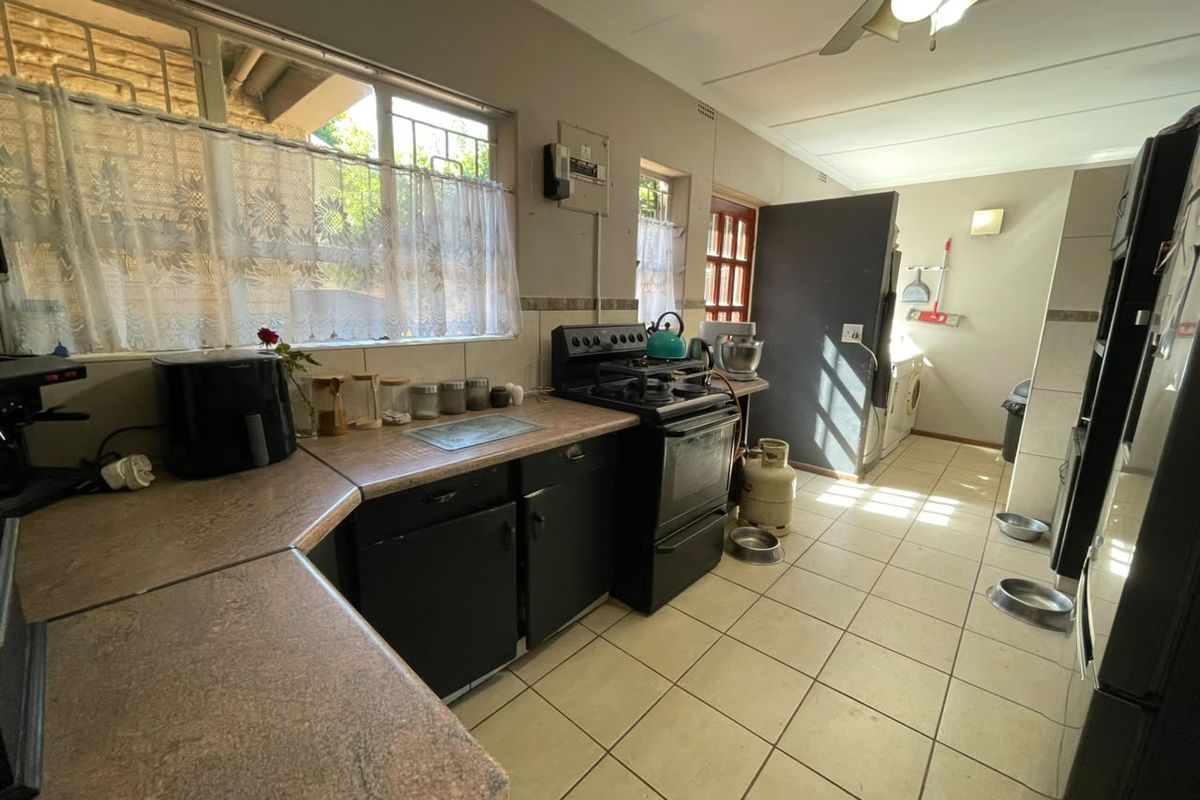 A functional kitchen featuring laminate countertops, built-in cabinetry, and a gas stove, with tiled flooring and direct access to a laundry area.