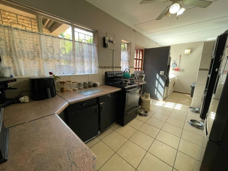 A functional kitchen featuring laminate countertops, built-in cabinetry, and a gas stove, with tiled flooring and direct access to a laundry area.