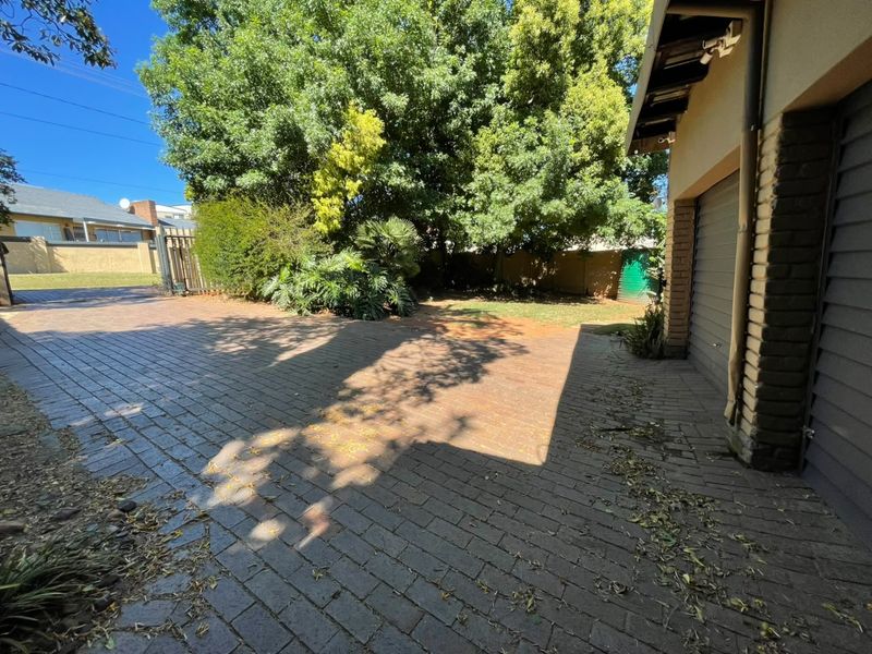 A paved driveway leading to a garage, featuring mature trees and a boundary wall in a residential setting.