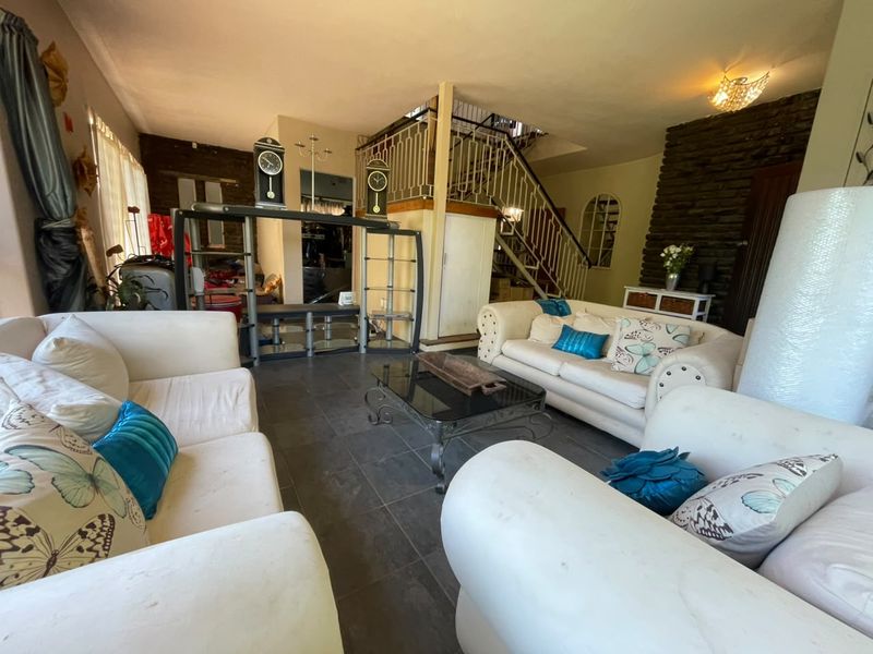Spacious living area featuring a stone accent wall, tiled flooring, and an open staircase with a decorative wrought iron balustrade.