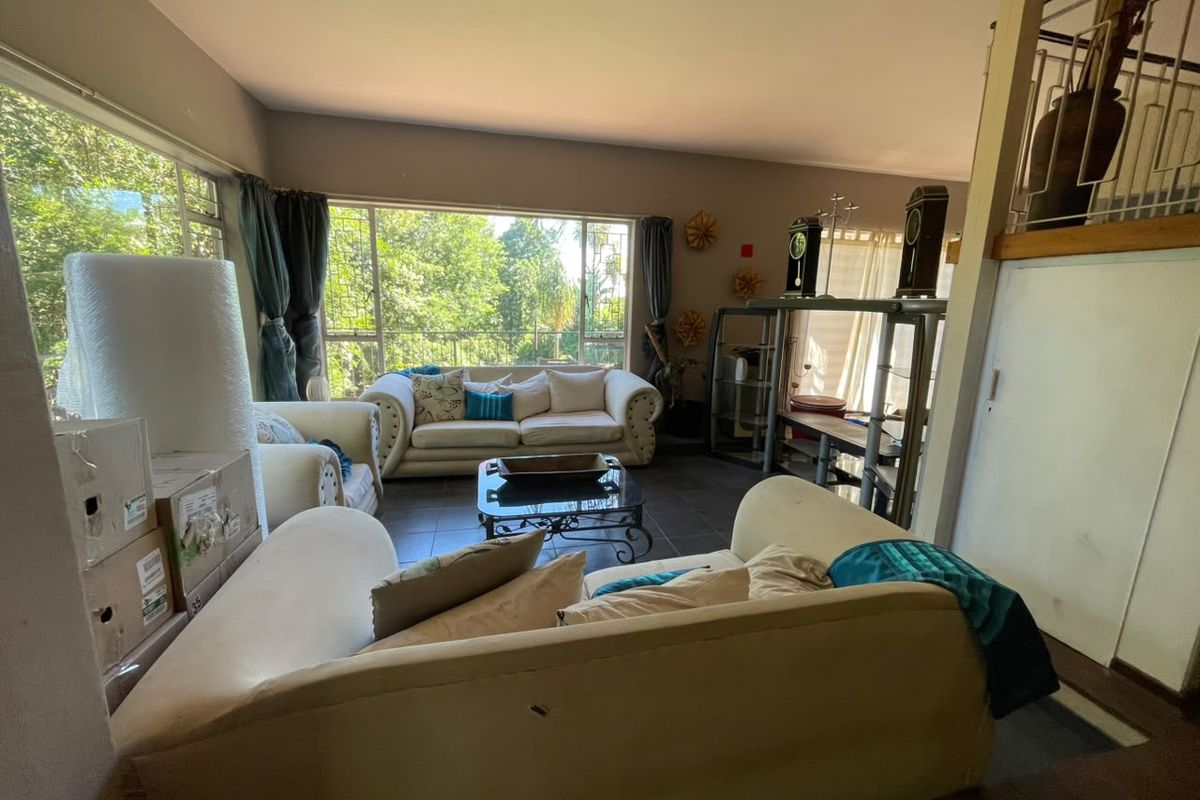 Spacious living room featuring large windows that provide ample natural light and views of the surrounding greenery, complemented by tiled flooring.