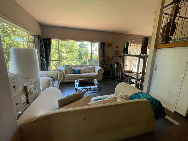 Spacious living room featuring large windows that provide ample natural light and views of the surrounding greenery, complemented by tiled flooring.