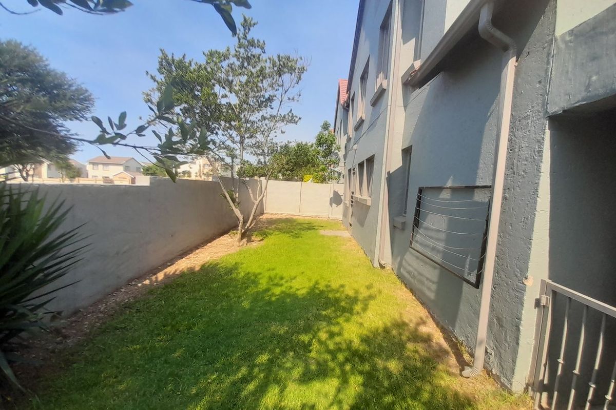 A rear exterior view of the townhouse featuring a small lawn, boundary wall, and wall-mounted drying rack attached to the building facade.
